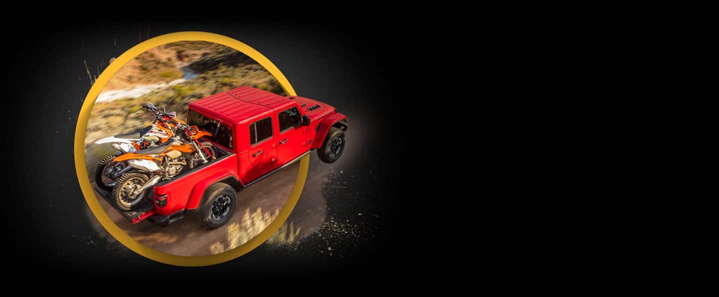 Una Jeep Gladiator Rubicon 2024 roja trasladando dos motocicletas todoterreno en la plataforma de la camioneta.