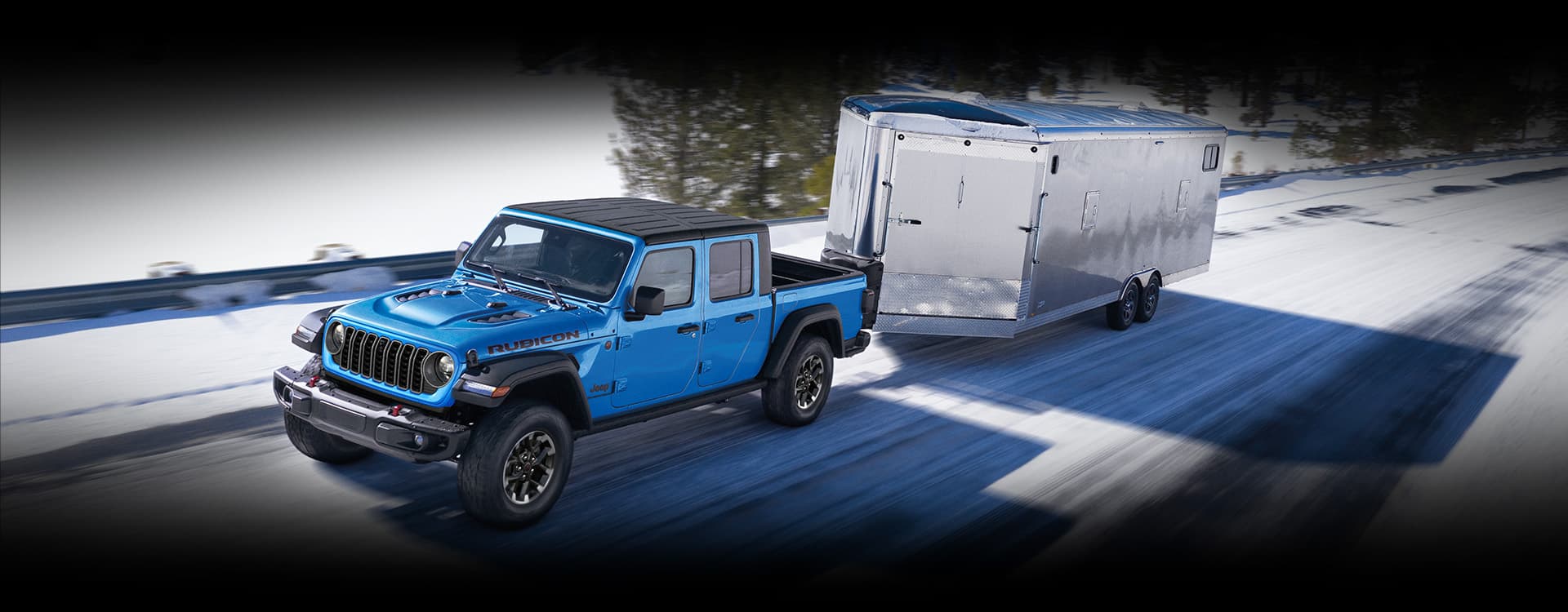 Una Jeep Gladiator Rubicon 2024 azul circulando por una carretera cubierta de nieve mientras acarrea un remolque cerrado.