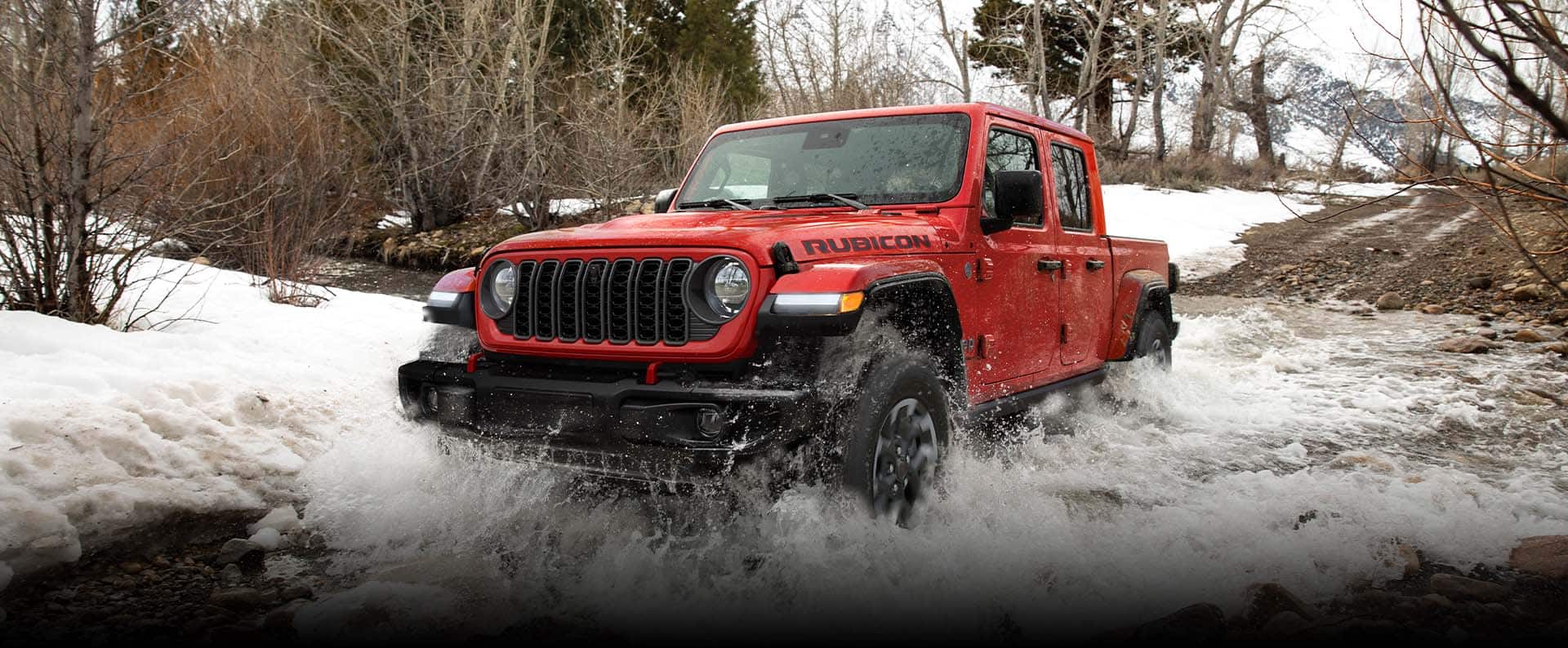 A red 2024 Jeep Gladiator Rubicon X fording through an icy stream off-road. The Black Friday Sales Event. Gladiator.