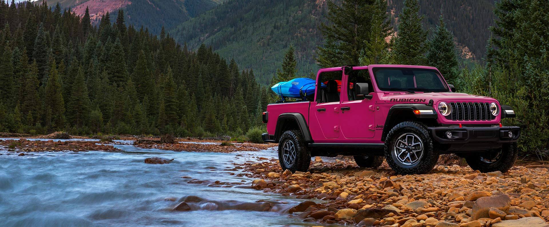 a pink truck parked on rocks next to a river