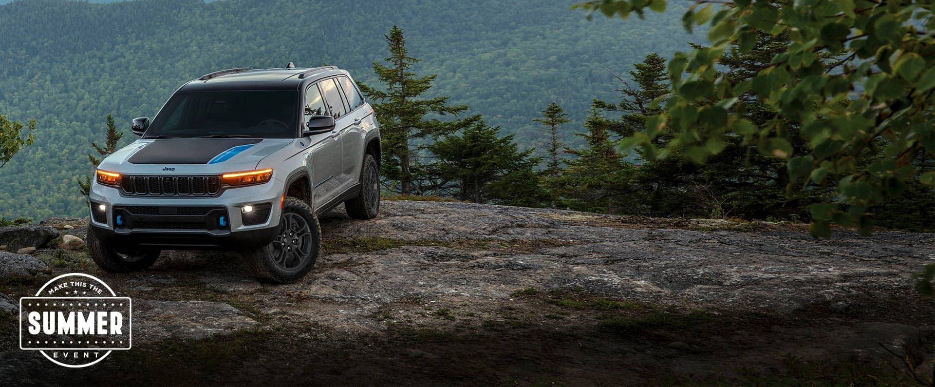 Un Jeep Grand Cherokee Trailhawk 2024 plateado con inserción negra en el capó, estacionado en el borde de un precipicio, en las montañas. Conviértelo en el evento del verano.