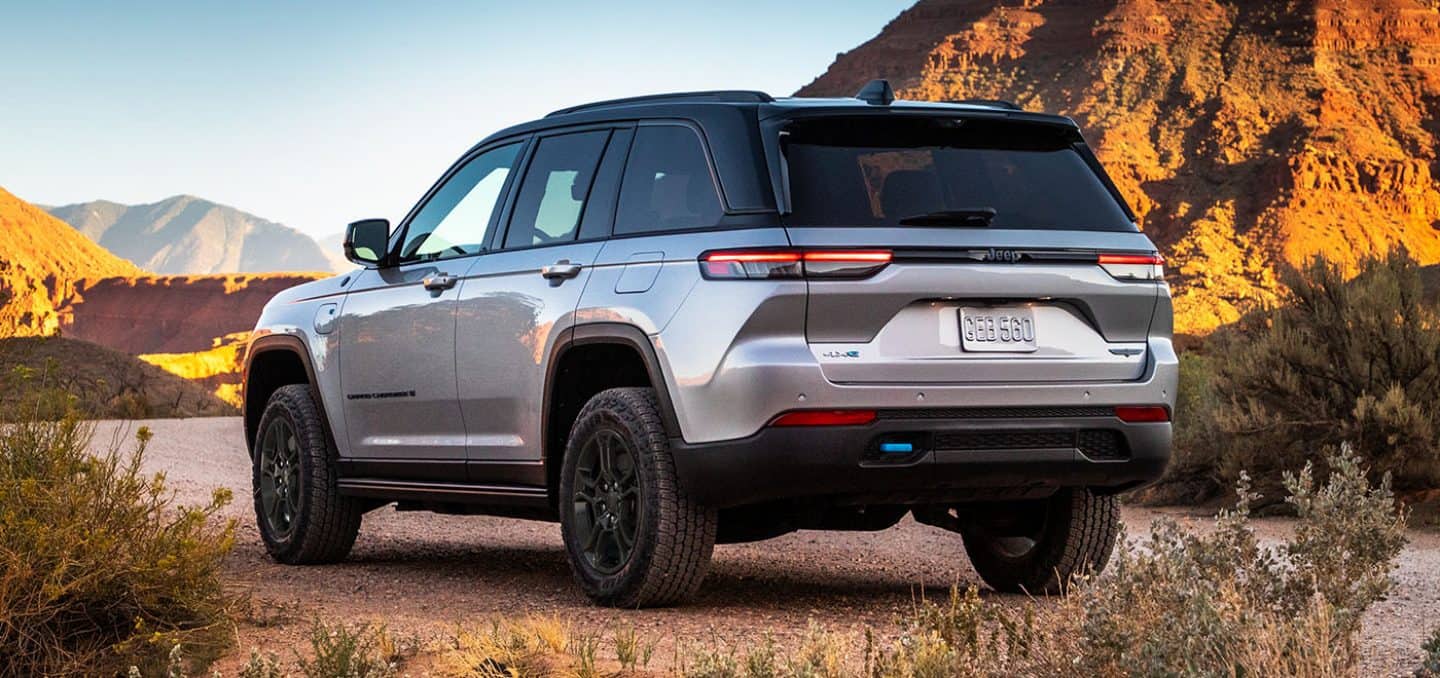 Display A silver 2024 Jeep Grand Cherokee Trailhawk 4xe parked on a clearing off-road, surrounded by hills of stone.