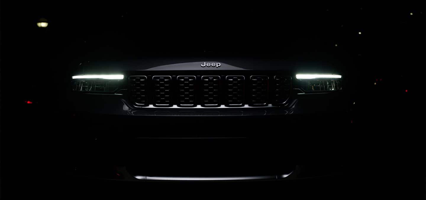 Display The entire 2025 Jeep Grand Cherokee Summit Reserve shrouded in darkness except for the grille and headlamps.