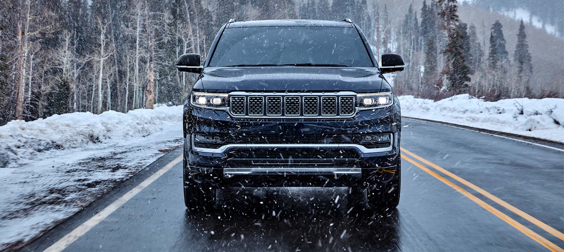 A head-on angle of a black 2024 Grand Wagoneer Series III being driven on a highway in a snowstorm.