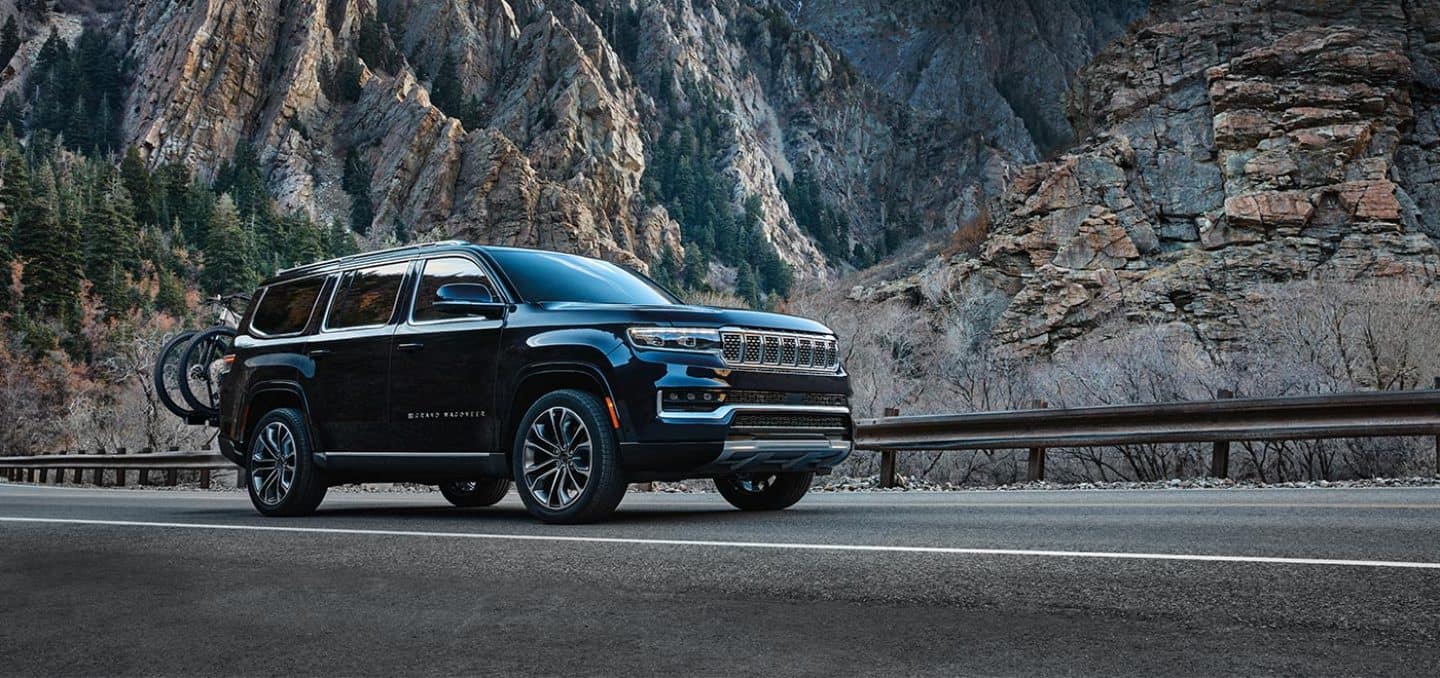 Display A black 2024 Grand Wagoneer Series III parked on a mountain road beside a steep rock face.