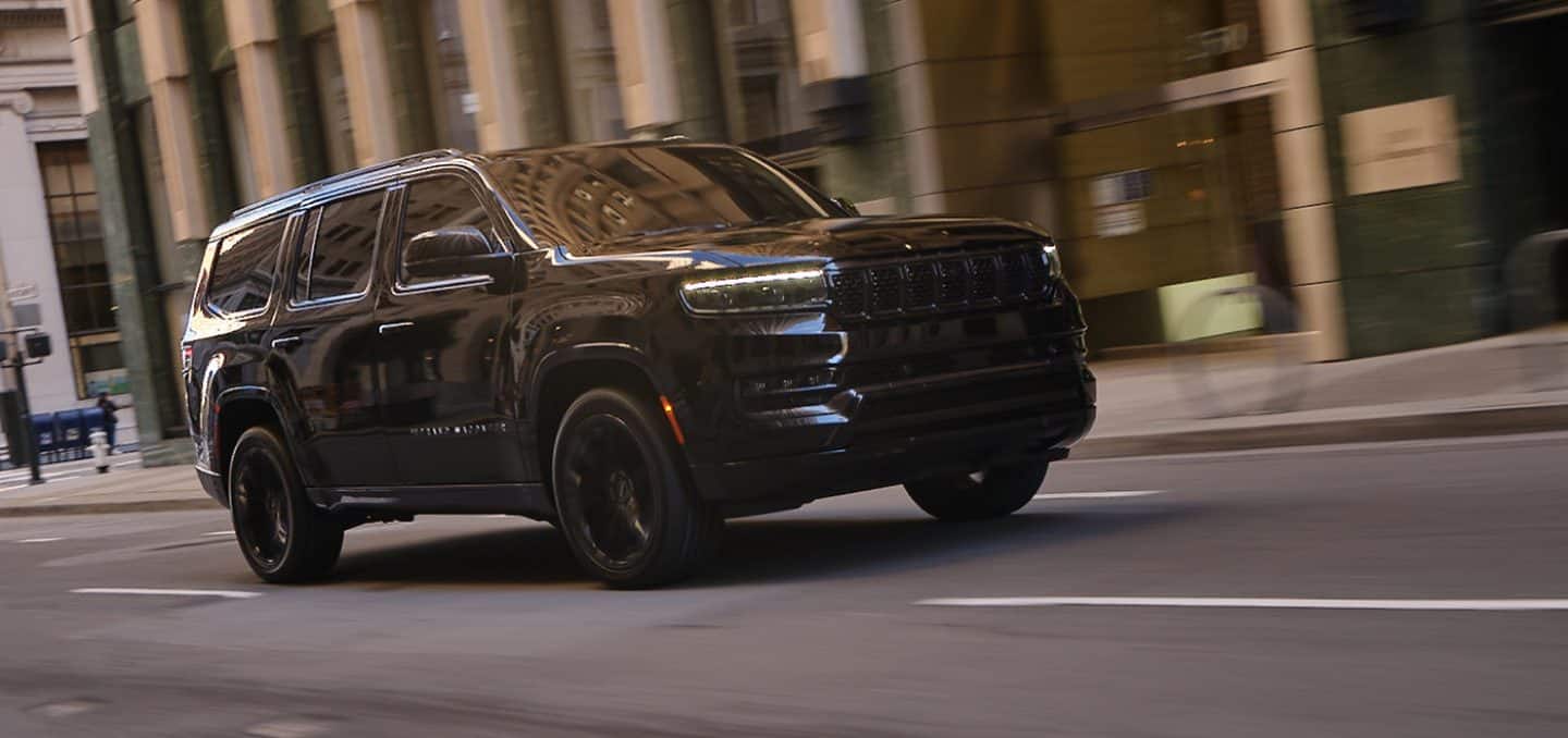 Display The 2024 Grand Wagoneer with the Obsidian Package, all in black, being driven down a city street.