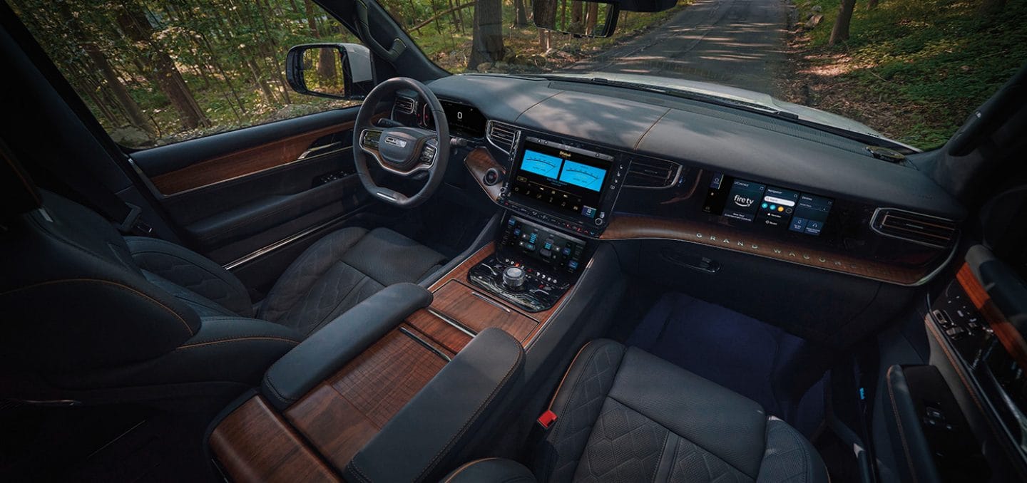 Display The front row of the 2024 Grand Wagoneer Series III cabin, highlighting the seats, steering wheel, Uconnect touchscreen, Articulating Lower Comfort Display and Passenger Interactive Display.