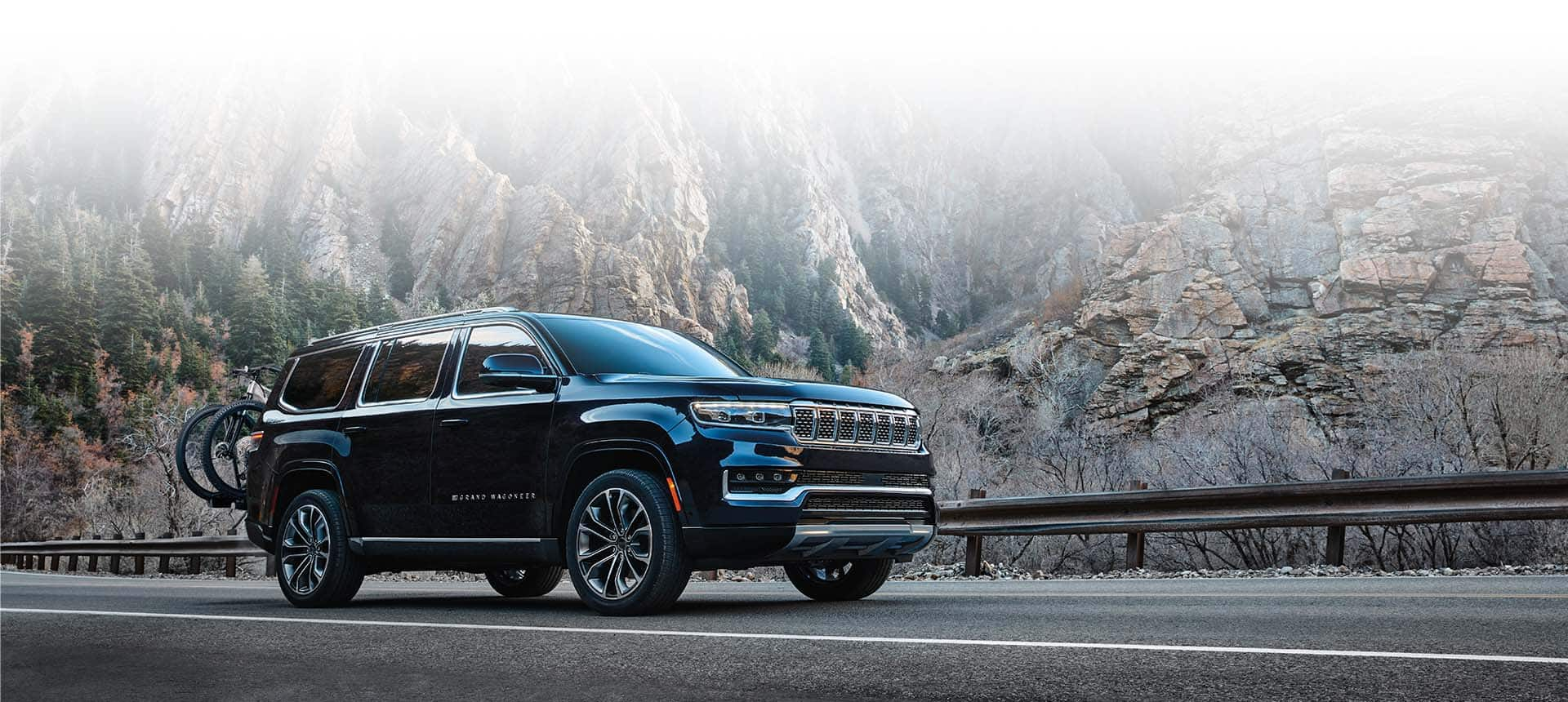 A black 2024 Grand Wagoneer Series III parked on a mountain road beside a steep rock face.