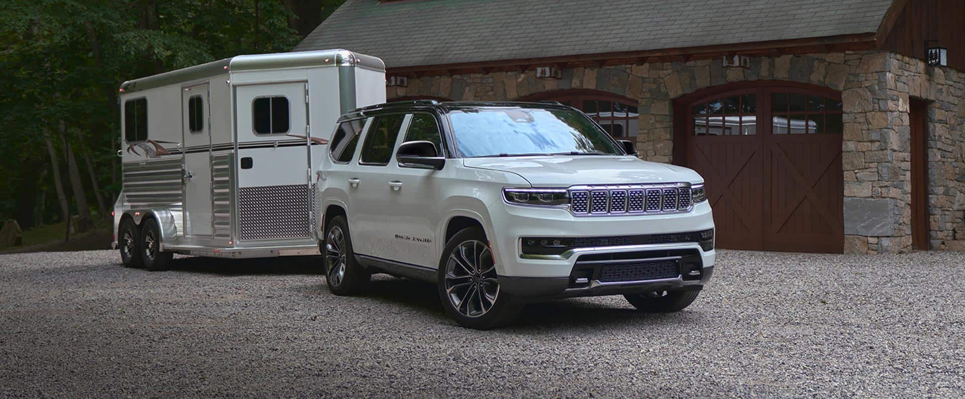 Un Jeep Wagoneer S Launch Edition 2024 blanco con un techo negro, estacionado al lado de un edificio de ladrillos, con un hombre caminando hacia el vehículo.