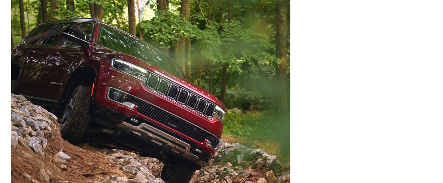 A red 2024 Wagoneer crawling over an uneven surface off-road.