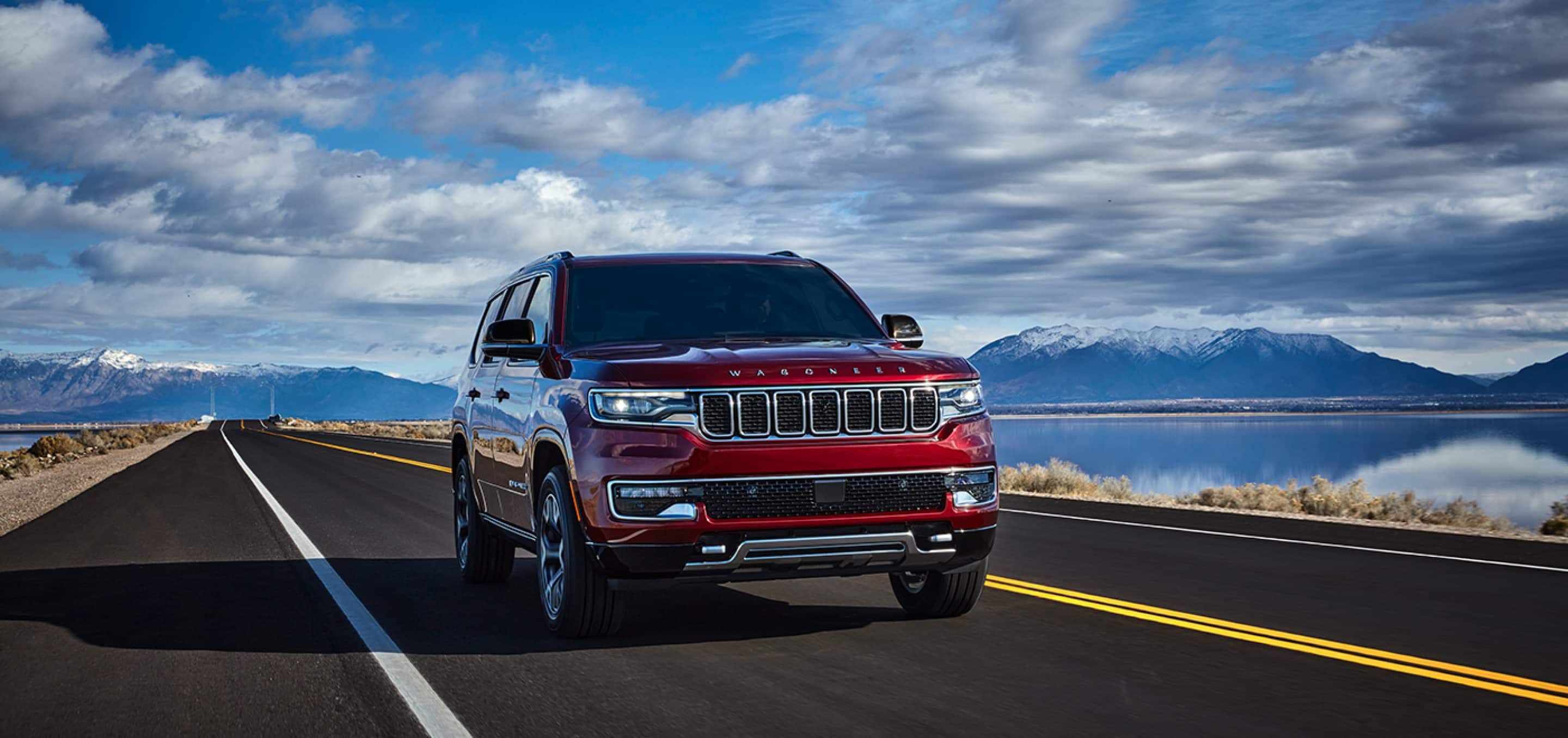 2024 Jeep Wagoneer in Velvet Red Pearl driving on lakeside road.