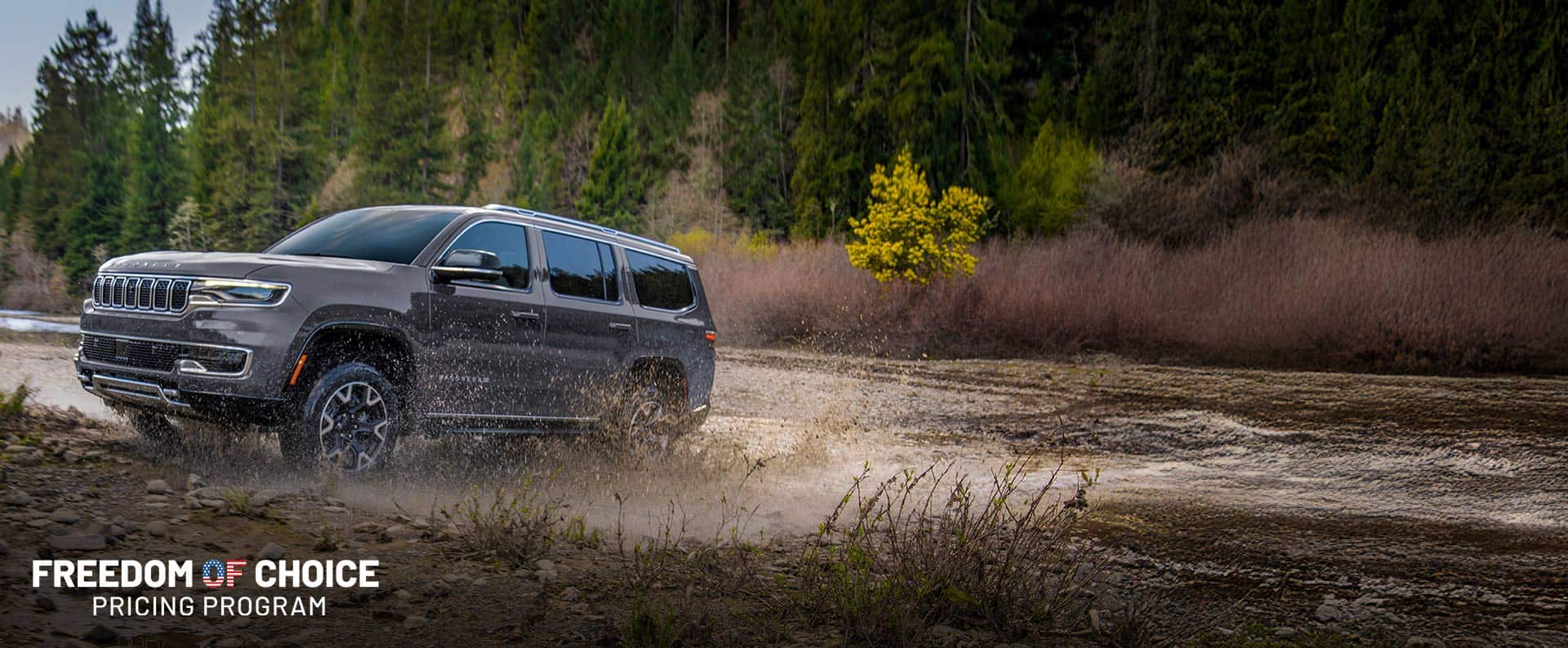 A grey 2024 Grand Wagoneer L Series 3 exiting a muddy stream off-road. Freedom of Choice Pricing Program event.