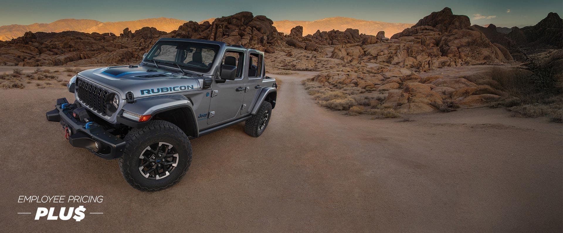 Un perfil desde el ángulo del conductor de un Jeep Wrangler Rubicon 4xe 2024 gris estacionado en un claro en el desierto. Evento de precios de empleado.