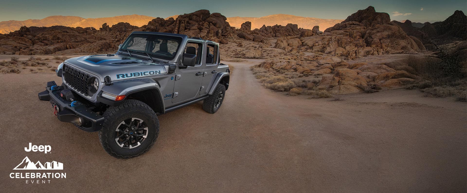 Un perfil desde el ángulo del conductor de un Jeep Wrangler Rubicon 4xe 2024 gris estacionado en un claro en el desierto. Evento de celebración de Jeep.