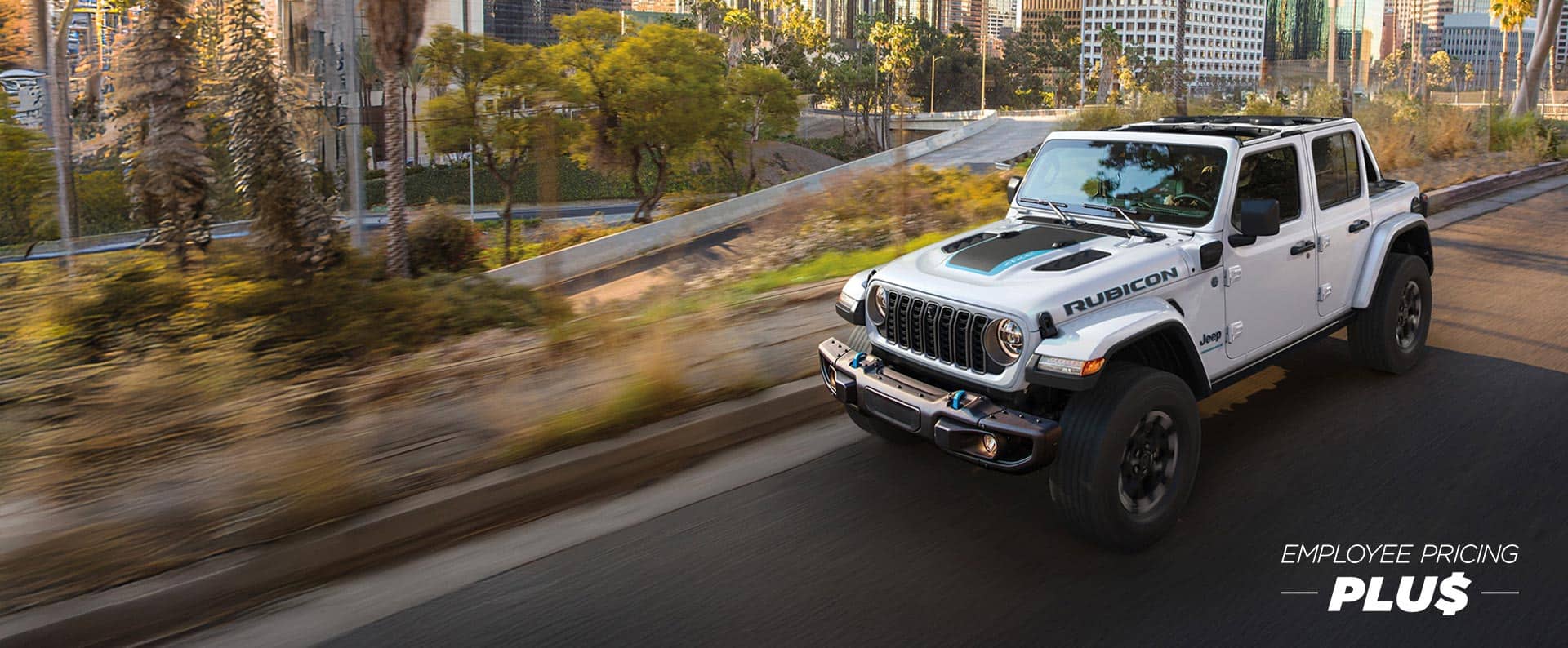 A white 2024 Jeep Wrangler Rubicon X 4xe with black hood insert, traveling on a city street with tall buildings in the background. Employee Pricing Plus event.
