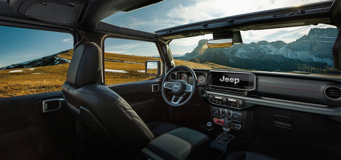 Display The interior of a 2025 Jeep Wrangler Rubicon, focusing on the driver seat, steering wheel, Uconnect toucscreen, dash, center stack controls and open sunroof.