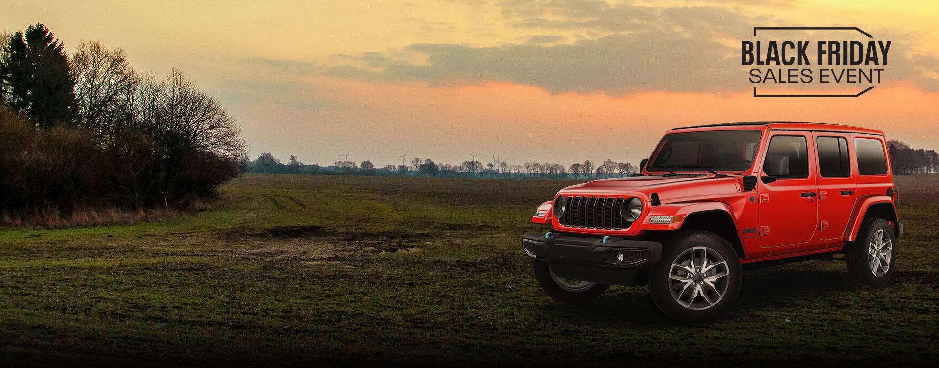 An angled driver-side profile of a red 2024 Jeep Wrangler Sport S 4xe parked in a grassy field at sunset. Black Friday Sales Event.