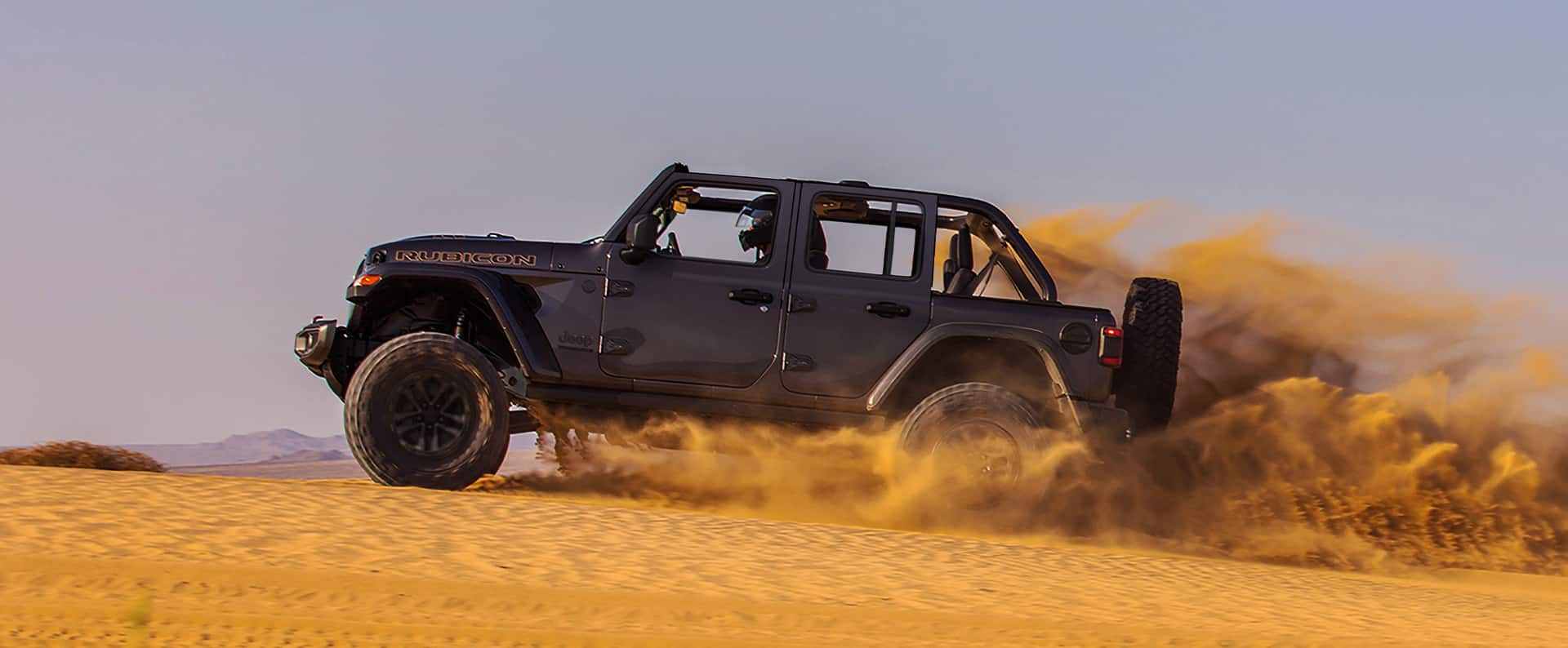 Un Jeep Wrangler Rubicon 392 2024 gris con el techo extraído circulando por el desierto, levantando arena mientras avanza.