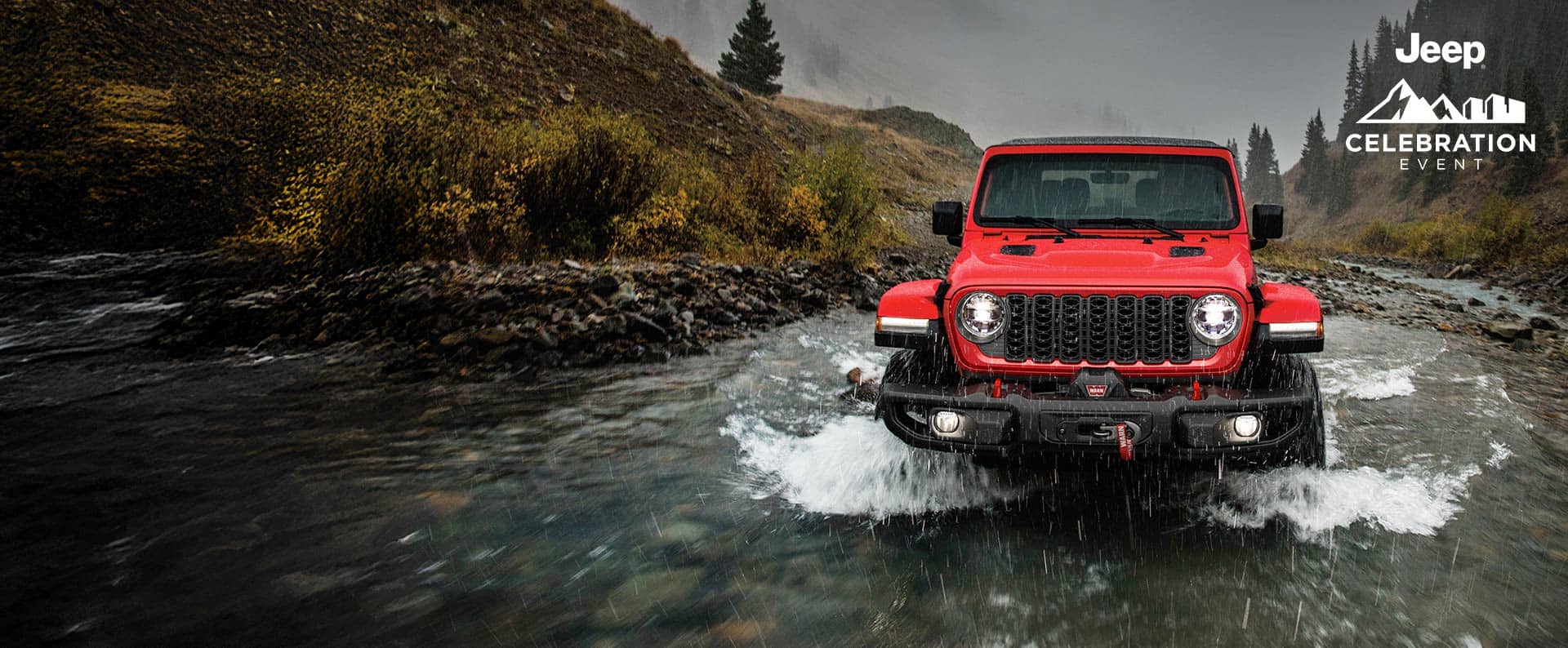 Ángulo frontal de un Jeep Wrangler Rubicon 2024 rojo que circula a través de un arroyo, siguiendo su camino. Evento de celebración de Jeep.