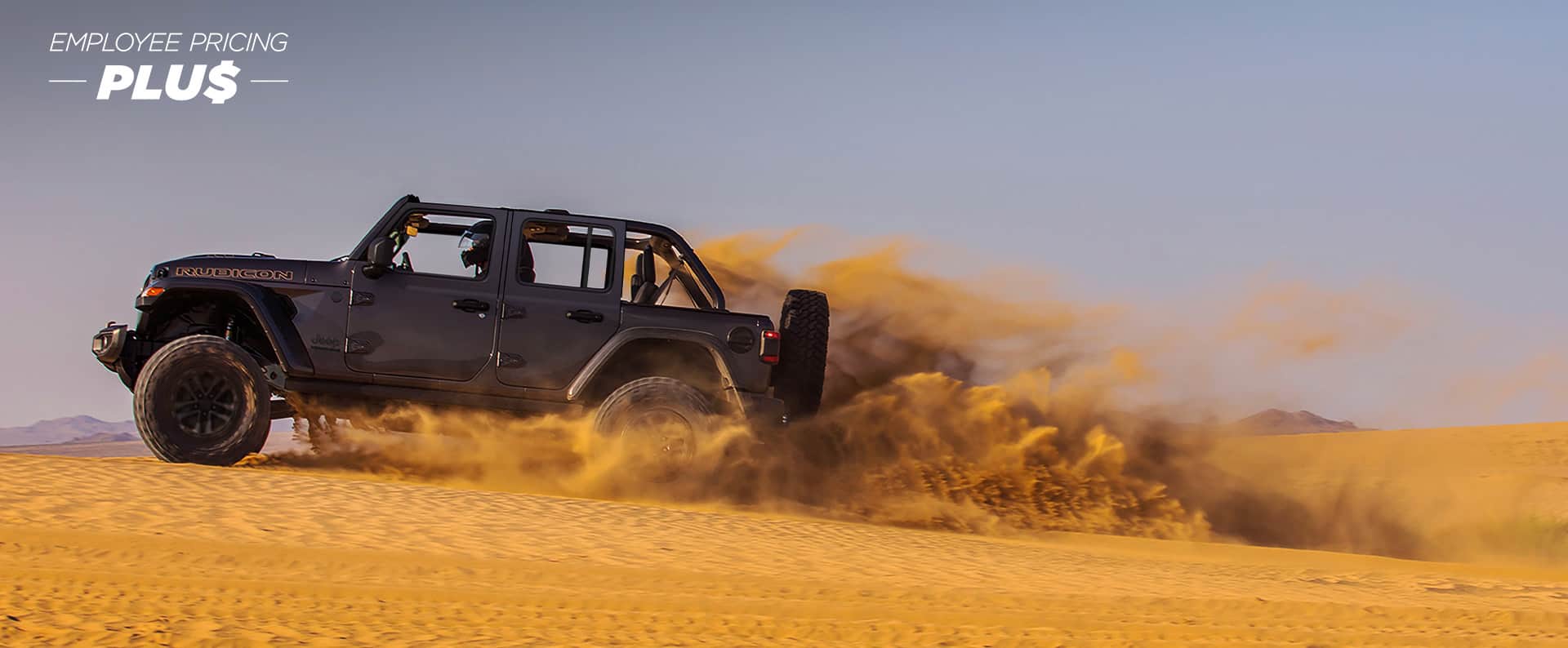 A gray 2024 Jeep Wrangler Rubicon 392 with its roof removed, traveling through the desert, kicking up sand as it goes. Employee Pricing Plus Event.