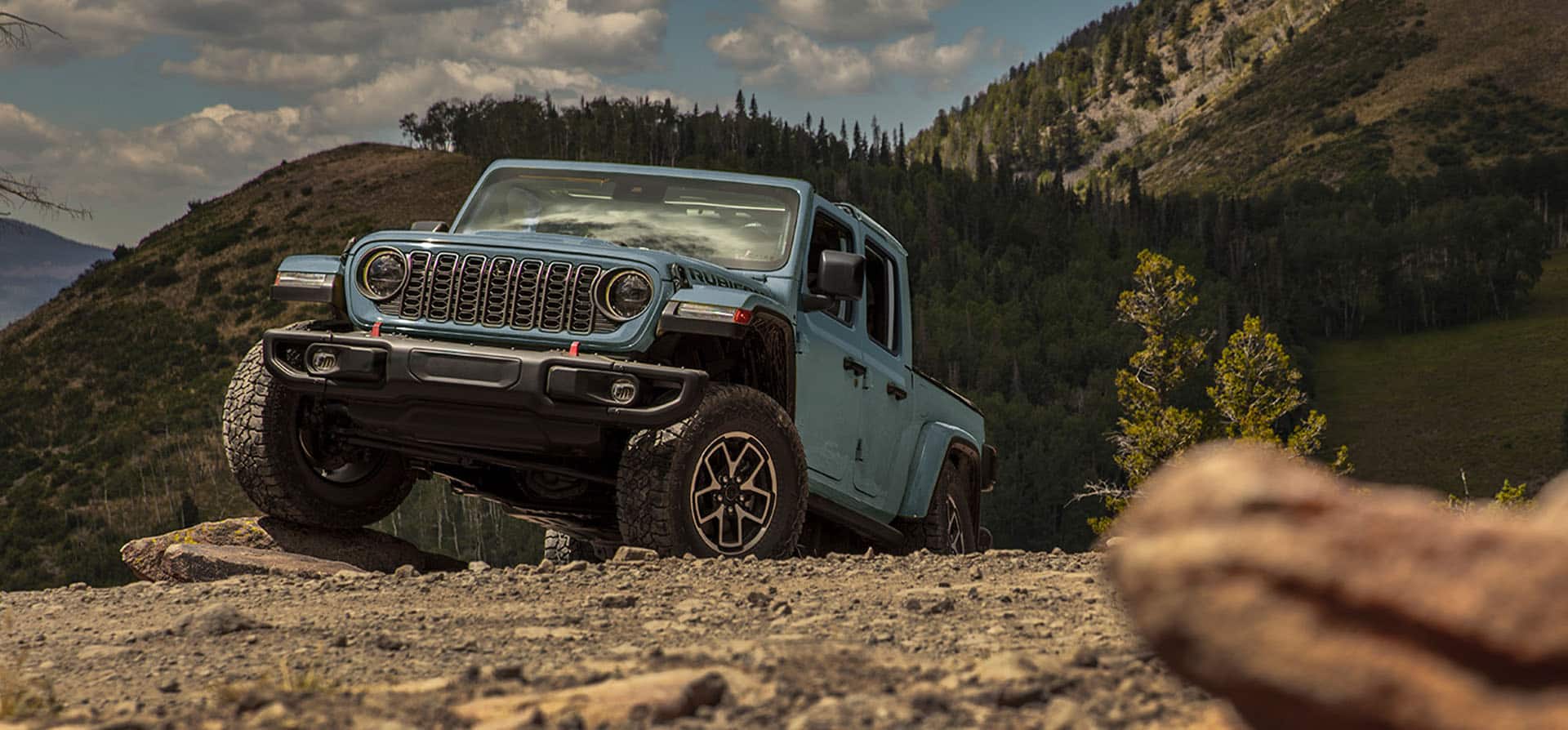 Un Jeep Gladiator Rubicon X 2025 roja ascendiendo por un sendero rocoso e irregular todoterreno con un Jeep Gladiator Rubicon X 2025 verde oliva detrás.