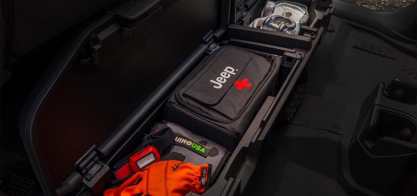 Display The lockable rear seat storage in the 2025 Jeep Gladiator with the removeable under seat storage bin filled with a Jeep Brand first aid kit and a variety of tools.