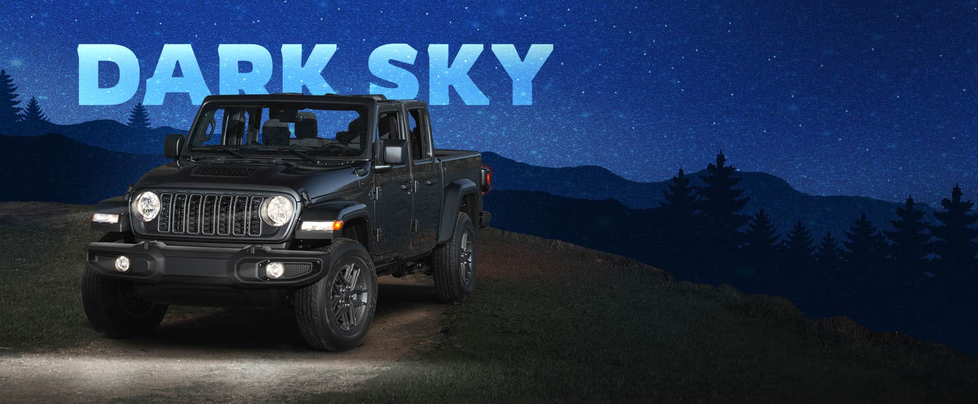 A front driver-side angle of a dark gray 2025 Jeep Gladiator Sport S with the Dark Sky Package on a dirt road with its headlamps on and its roof removed. Dark Sky.