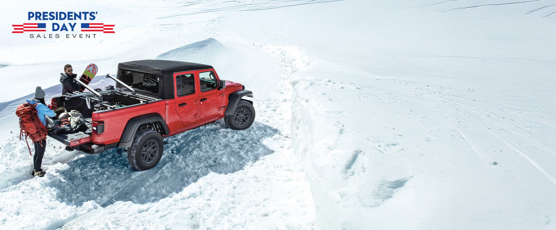 A red 2025 Jeep Gladiator Sport S with black soft top, parked in the snow with a couple removing winter sports equipment from the bed of the truck. The Presidents' Day Sales Event.