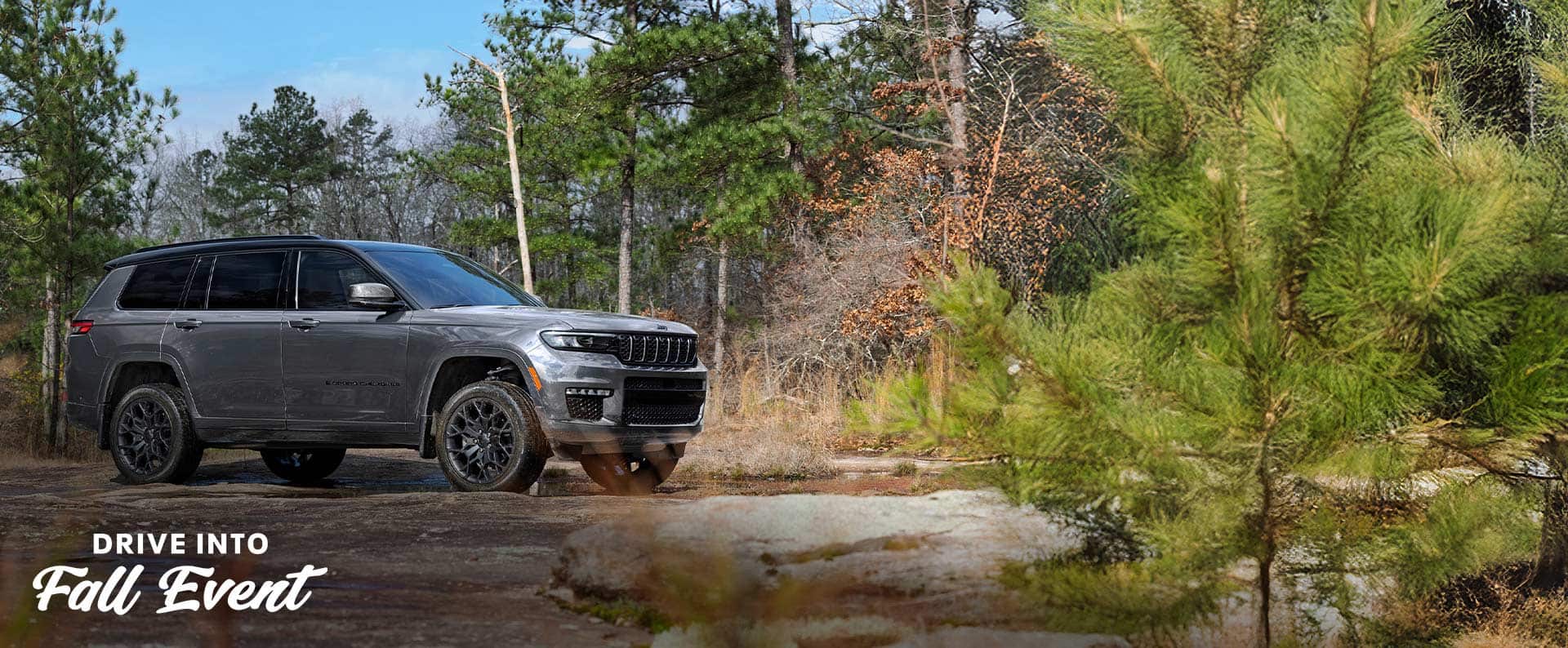 A passenger-side angle of a gray 2025 Jeep Grand Cherokee High Altitude parked on a trail off-road. Drive Into Fall Event.