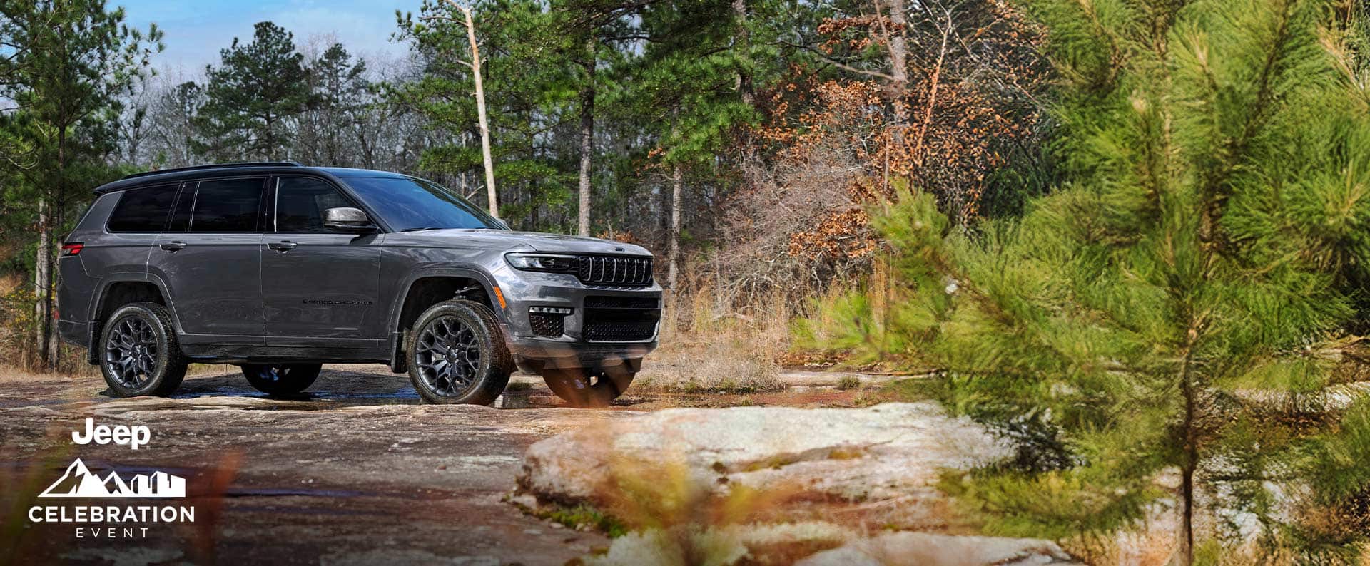 A gray 2025 Jeep Grand Cherokee L Summit Reserve High Altitude parked off-road beside a shallow, muddy stream. Jeep Celebration Event.