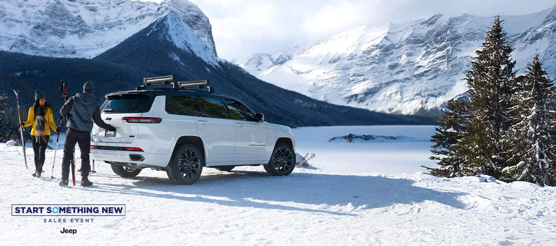 A white 2026 Jeep Grand Cherokee L High Altitude parked on a snow-covered clearing in the mountains. A couple nearby is carrying skiing equipment, and the man is about to open the liftgate. The Start Something New Sales Event. Jeep.