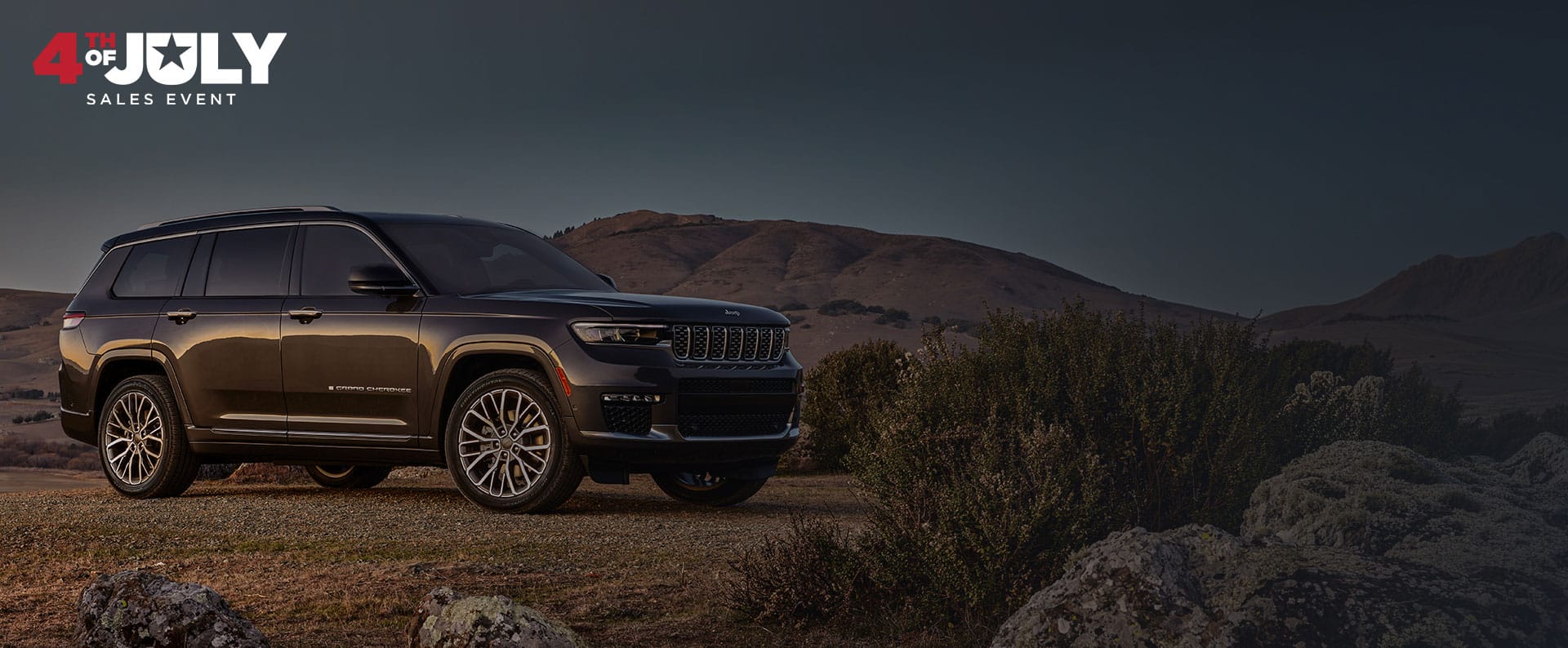 Un Jeep Grand Cherokee Summit Reserve 2025 gris oscuro estacionado en un claro fuera de la carretera, en el desierto. Evento de ventas del 4 de julio.