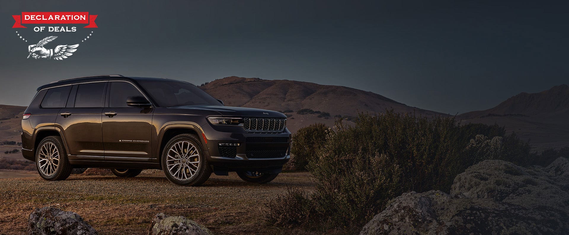 Ángulo delantero del lado del pasajero de un Jeep Grand Cherokee Summit Reserve 2025 gris estacionado en un claro fuera de la carretera. Declaration of Deals.