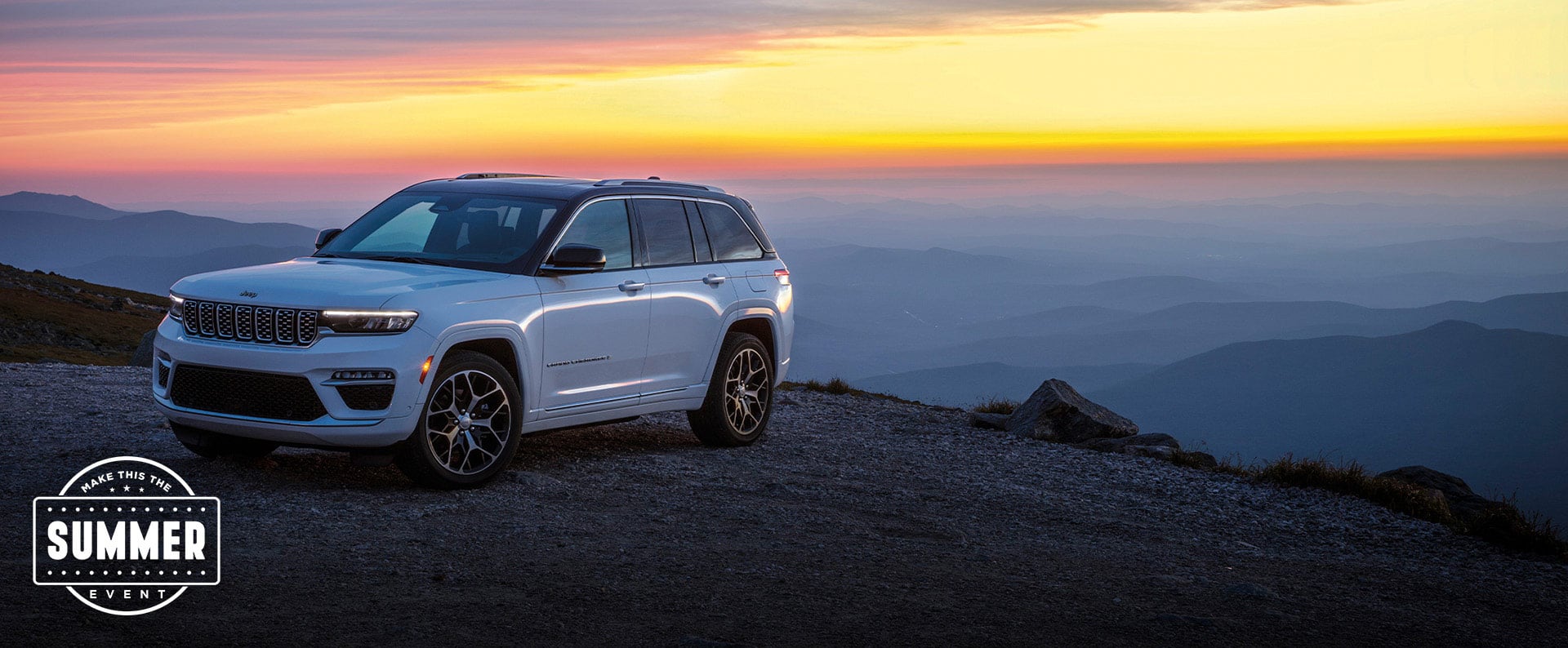 A white 2025 Jeep Grand Cherokee Summit Reserve parked near the edge of a cliff at sunset. Summer event.