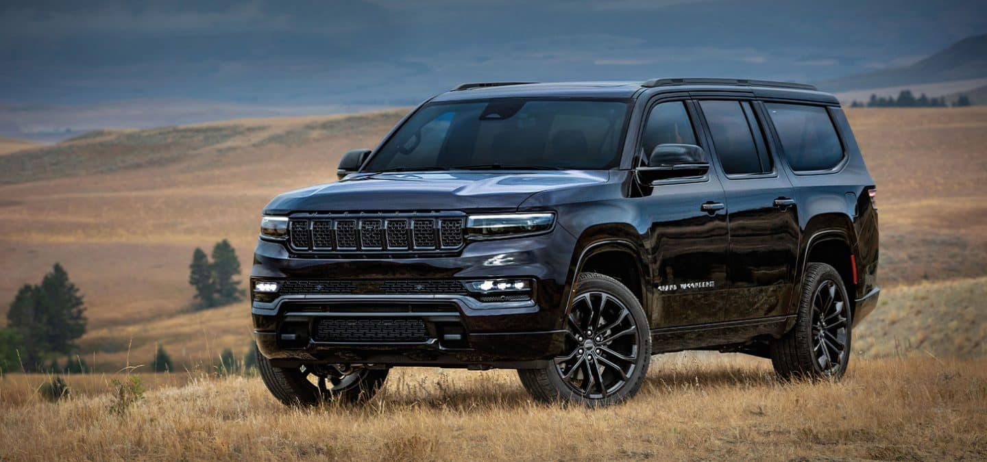 Display A driver-side front angle of a black 2025 Jeep Grand Wagoneer Obsidian parked in an open field in an area of hilly grasslands.