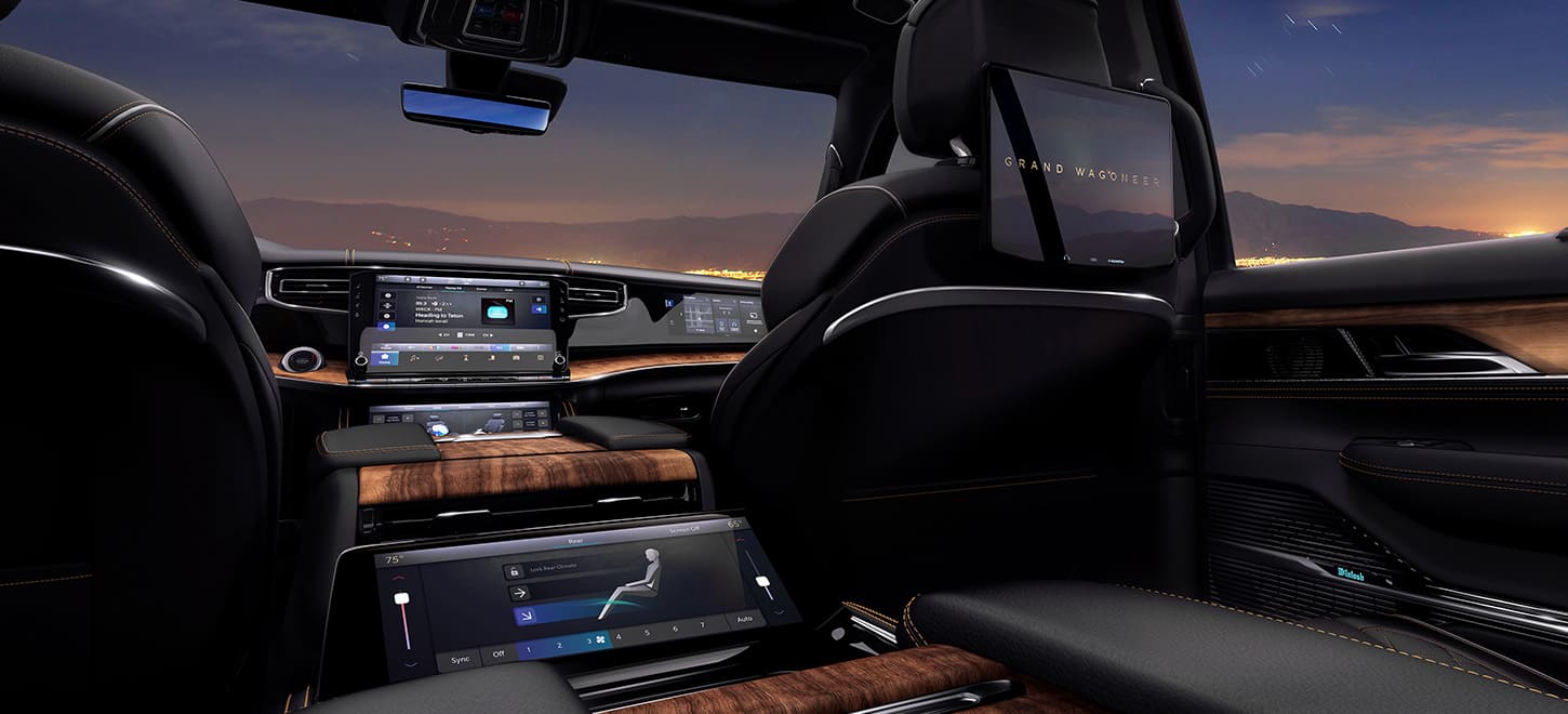The interior of the 2025 Jeep Grand Wagoneer Series 3  focusing on the Rear Comfort Display in the second row and the Uconnect touchscreen in the first row.