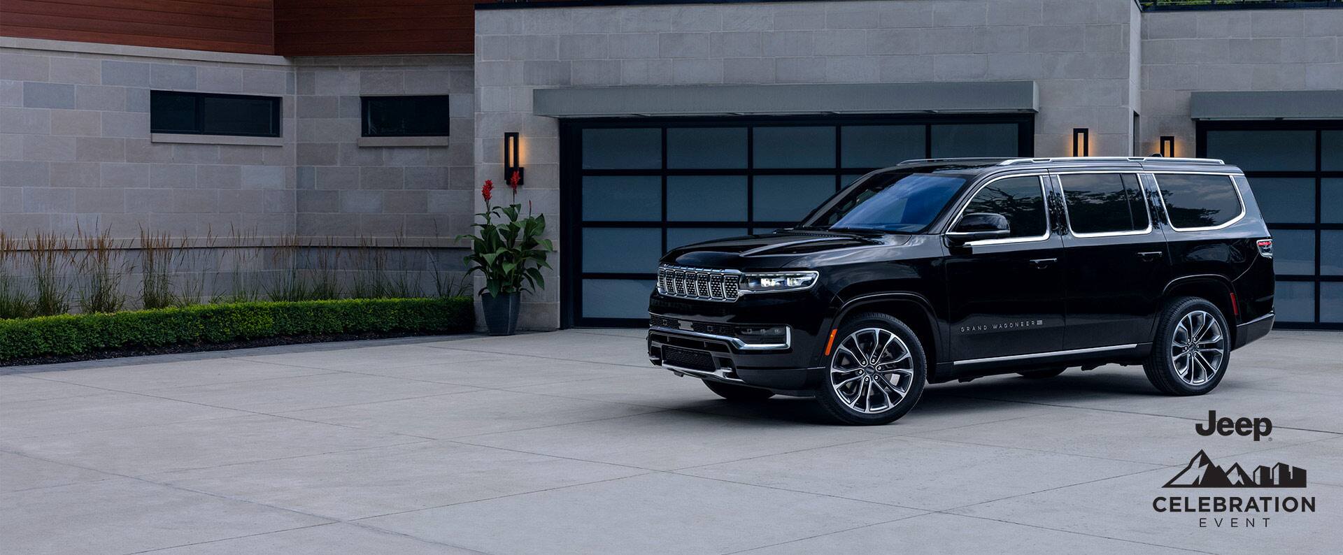 A black 2025 Jeep Grand Wagoneer Series 3 parked in the driveway of a large, modern home. Jeep Celebration Event.