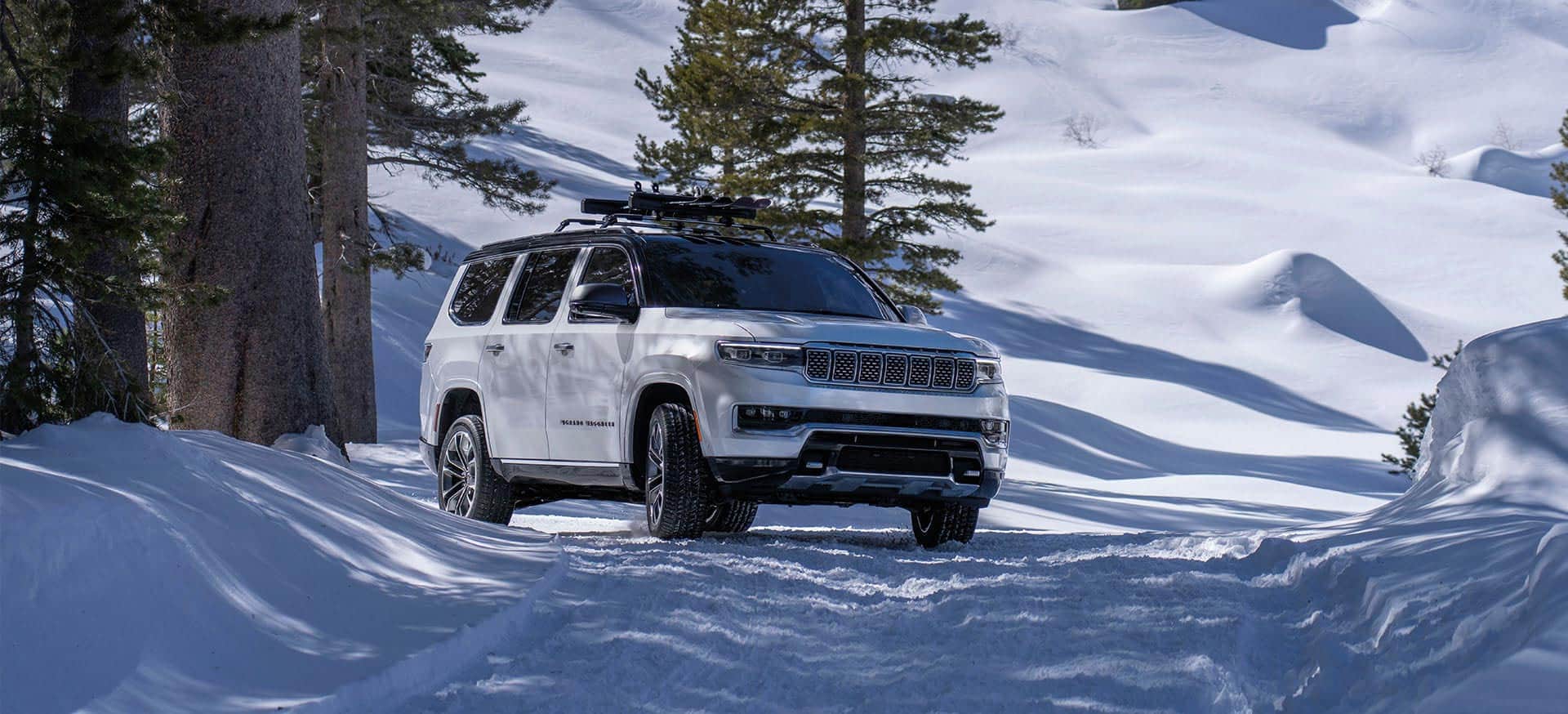A white 2025 Jeep Grand Wagoneer Series 3 traveling on a snow-covered trail in the mountains.