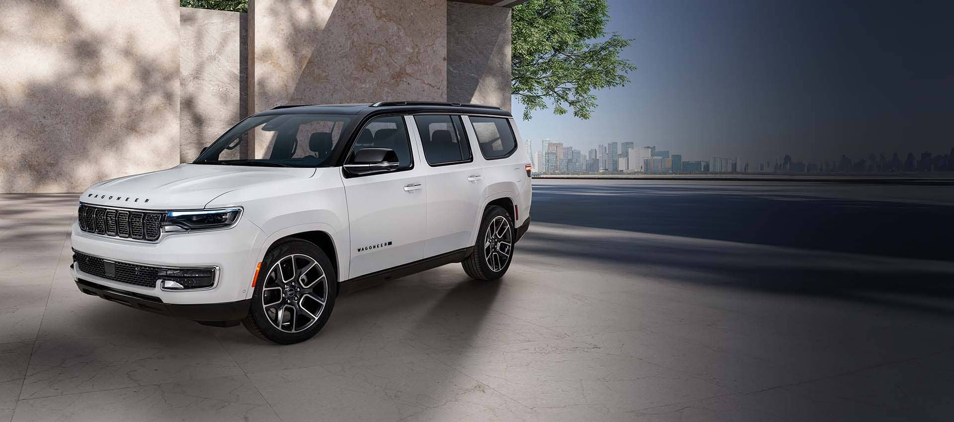 Ángulo delantero del lado del conductor de un Jeep Wagoneer Super 2025 blanco con techo negro, estacionado en la entrada para auto de un edificio moderno.