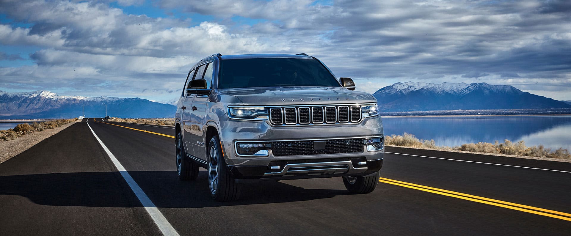 Un Jeep Wagoneer Series 3 2025 plateado circulando por una carretera al lado de un lago.