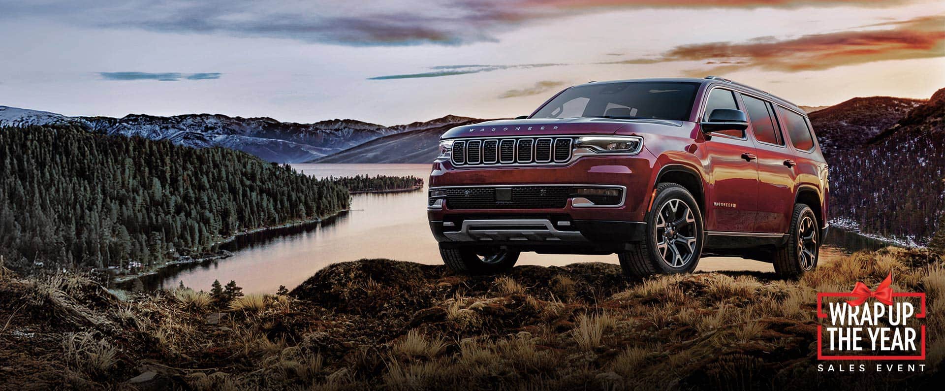 Un Jeep Wagoneer Series 3 2025 rojo en una colina cubierta de césped fuera de la carretera, con un lago y montañas de fondo. El evento Drive Into Fall.