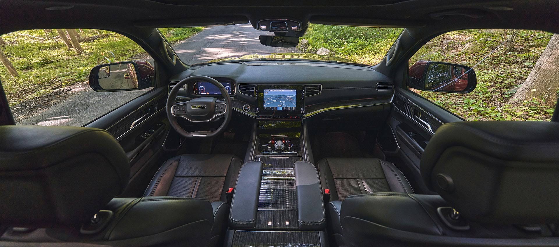 The front row of the 2025 Jeep Wagoneer Series III cabin, focusing on the seats, center console, steering wheel, Digital Cluster Display, Uconnect touchscreen center stack controls and dash.