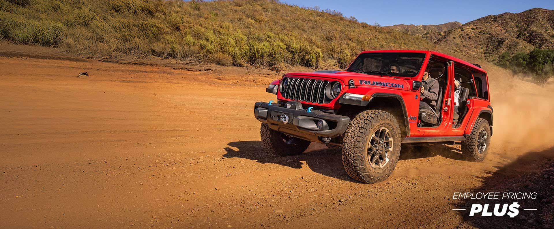 A red 2025 Jeep Grand Wrangler Rubicon X 4xe with its doors removed, climbing a sandy hill off-road. Employee pricing plus event.