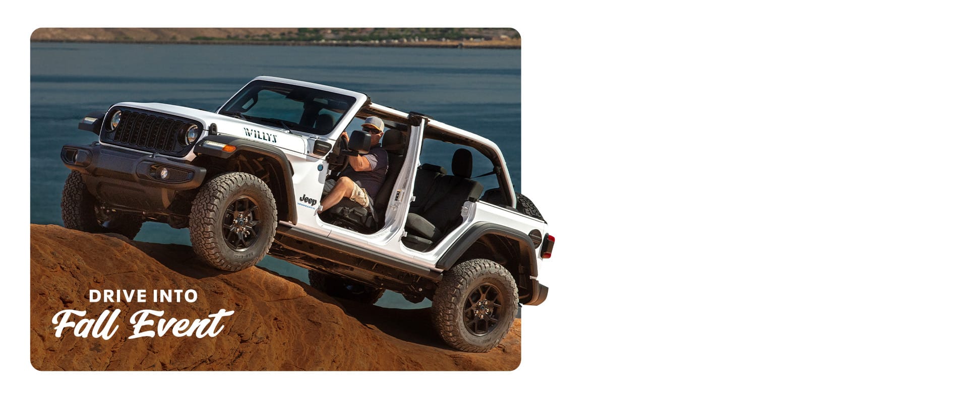 A white 2025 Jeep Wrangler Willys 4xe with its doors and top removed, ascending a sandstone hill. Drive Into Fall Event.