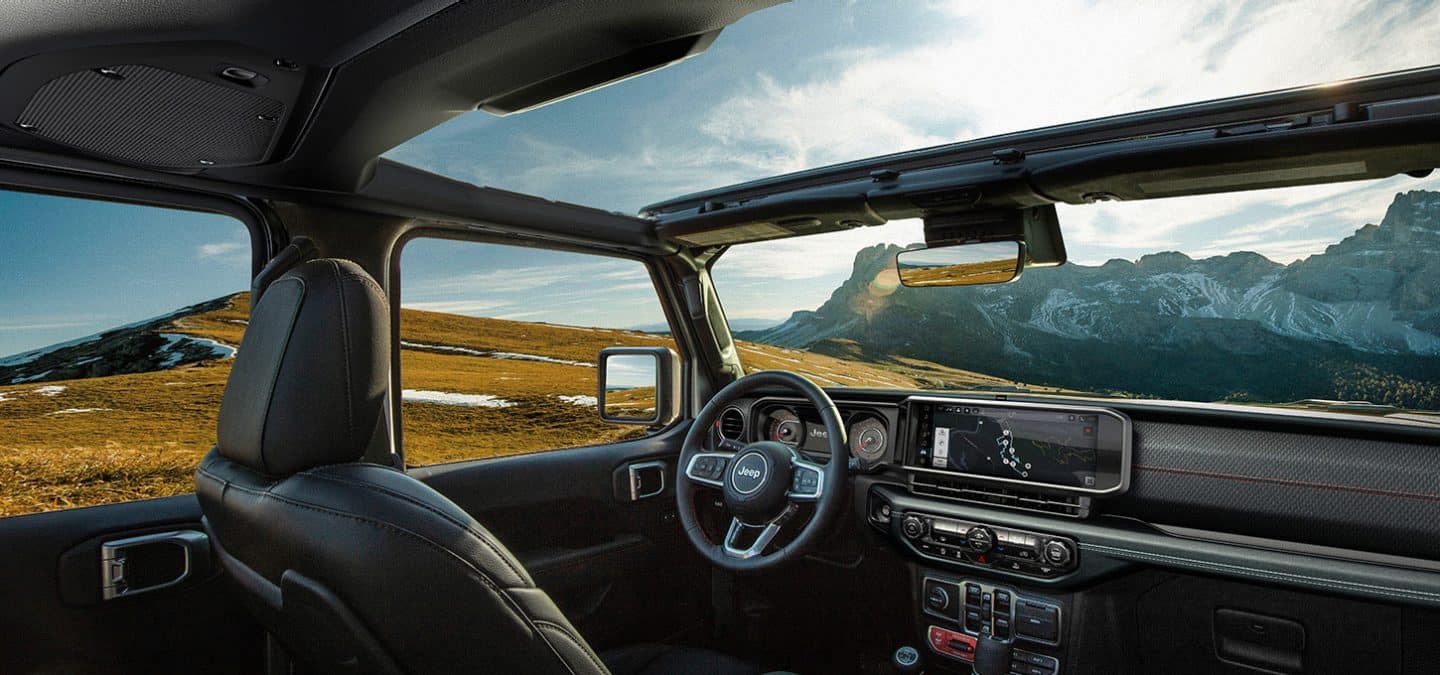 Display The front row in the 2025 Jeep Wrangler focusing on the open sunroof, steering wheel, Uconnect touchscreen and dash.