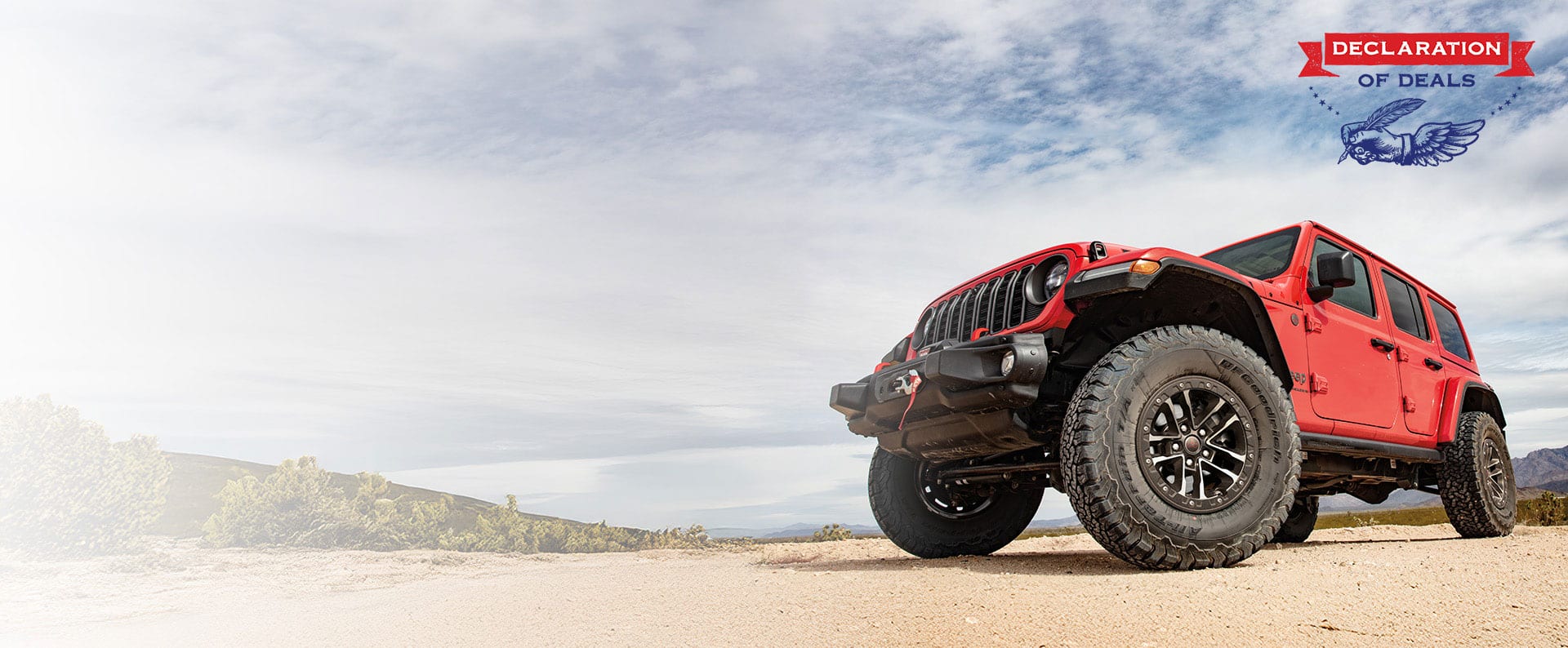 Ángulo frontal bajo de un Jeep Wrangler Rubicon X 2025 rojo viajando por un sendero arenoso fuera de la carretera. Declaration of Deals.
