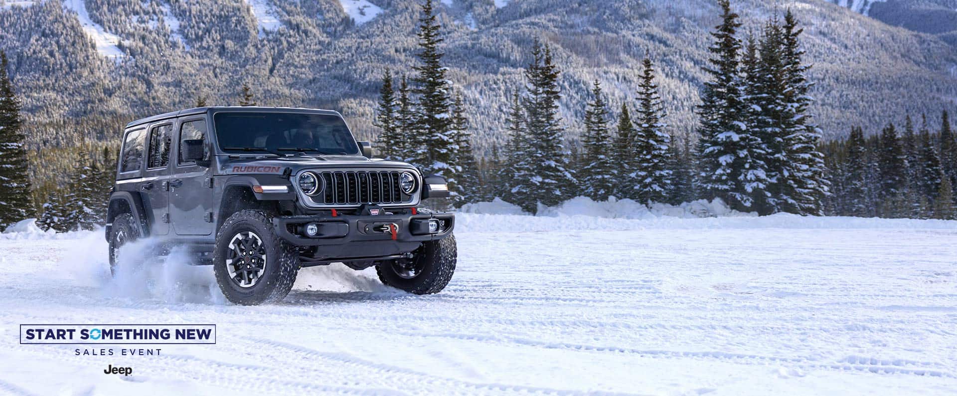 A dark gray 2025 Jeep Wrangler Rubicon traveling down a snow-covered trail with mountains in the background. The Start Something New Sales Event. Jeep.