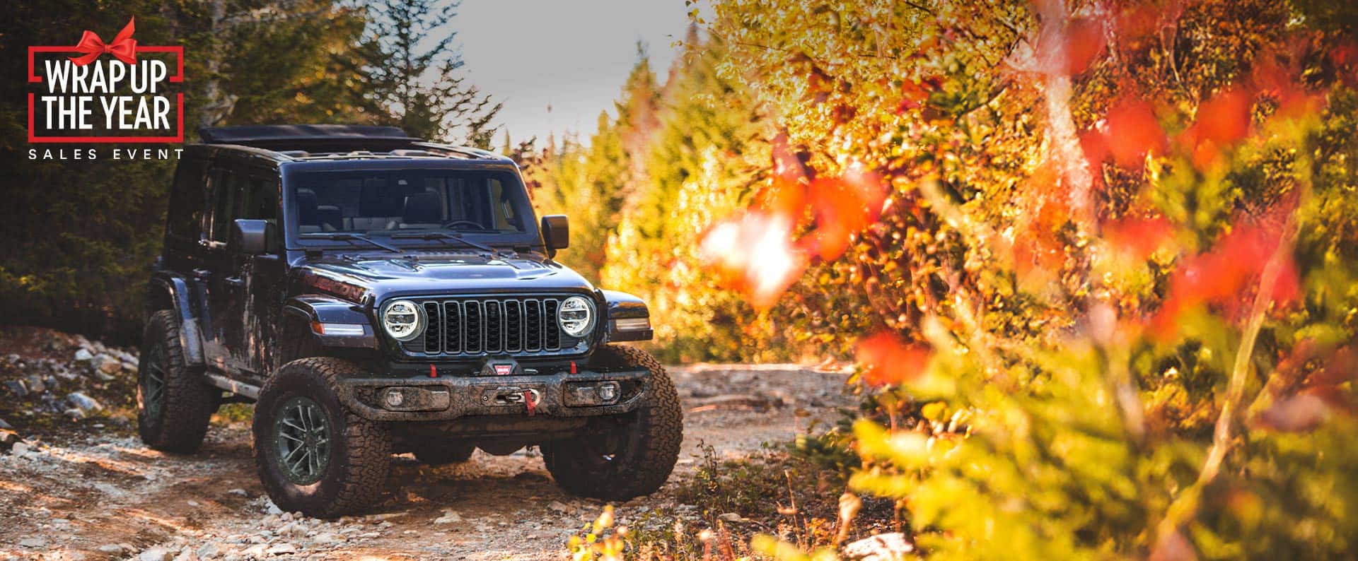 A black 2025 Jeep Wrangler Rubicon X parked on an off-road trail in the woods. The Drive Into Fall Event.