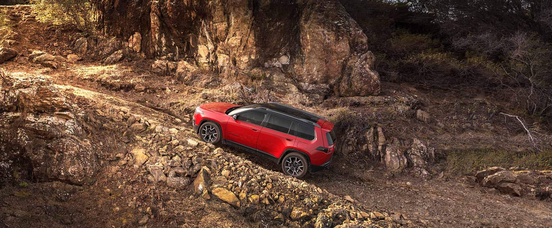 Perfil del lado del conductor de un Jeep Cherokee Overland 2026 rojo trepando un sendero pronunciado.