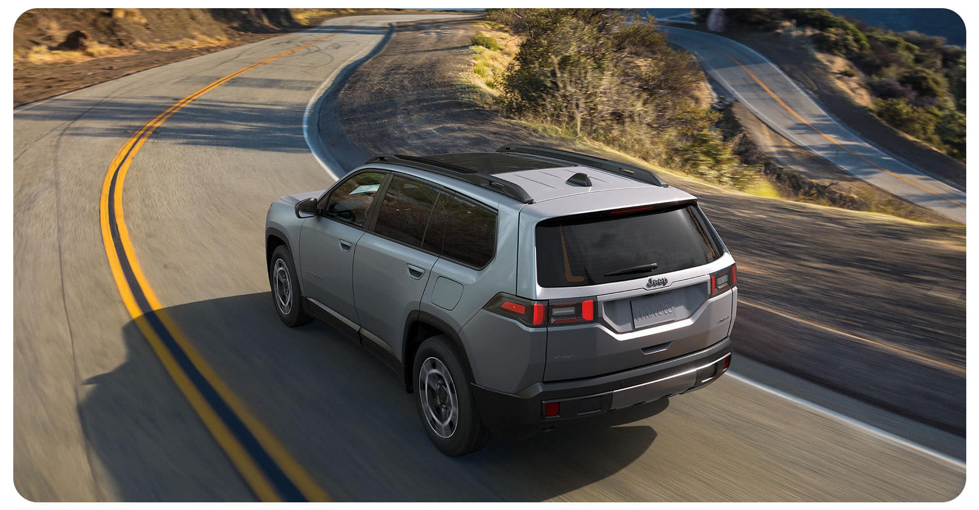 Ángulo trasero del lado del conductor de un Jeep Cherokee Limited 2026 plateado circulando por una carretera sinuosa.